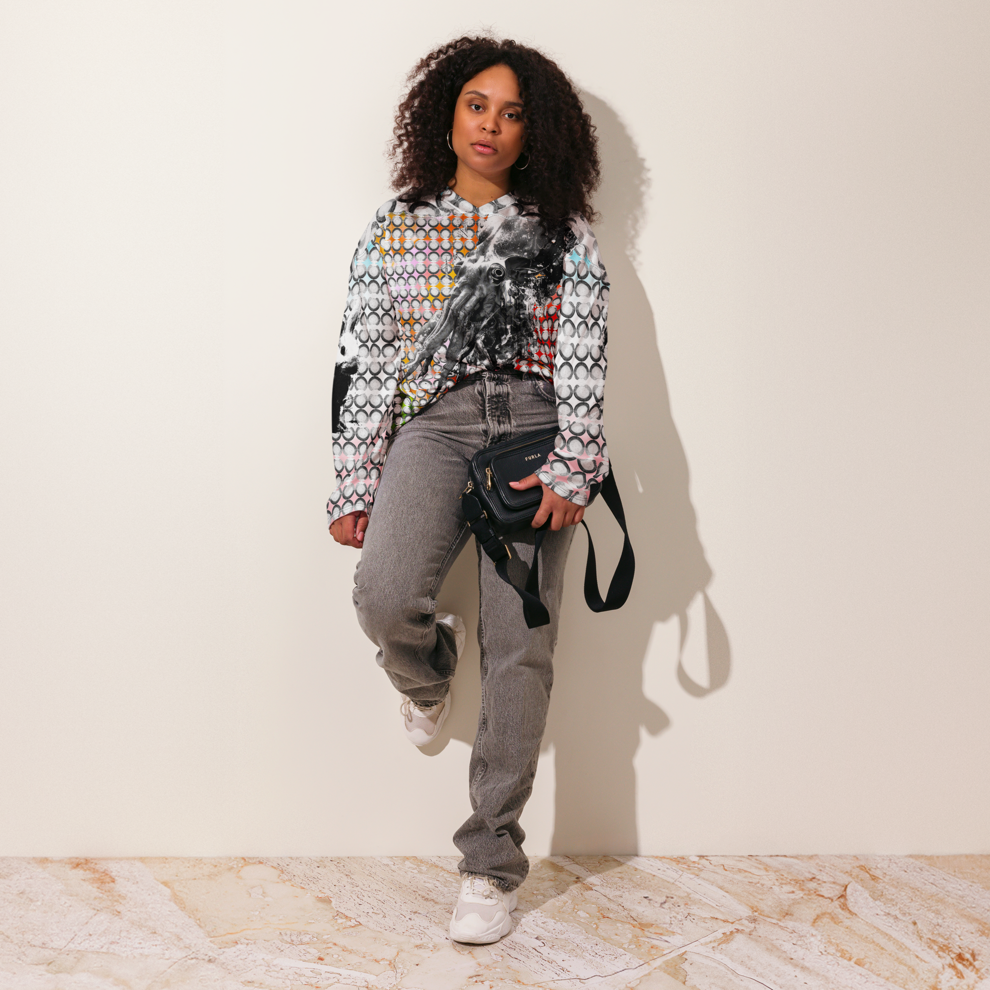 Woman wearing a patterned rthlng SKWIDEO JERSEY and gray jeans against a plain background